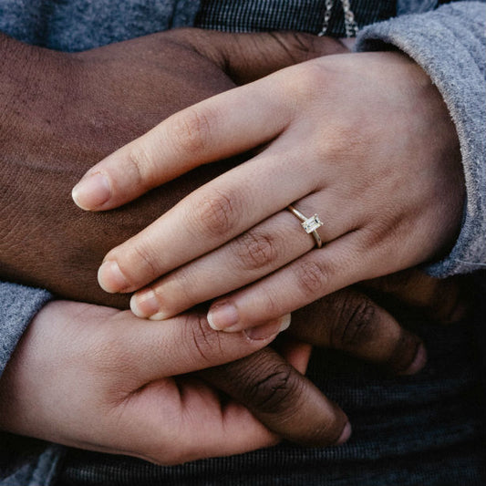 woman wearing yellow gold emerald cut engagement ring holding man's hand